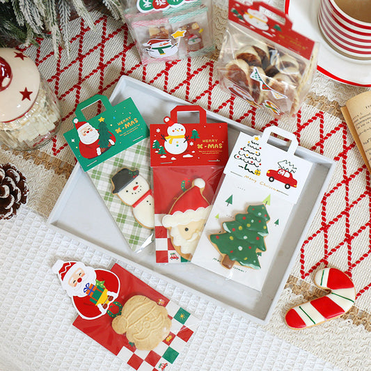Christmas biscuit gift bags with Santa, snowman and tree designs on a tray beside iced biscuits