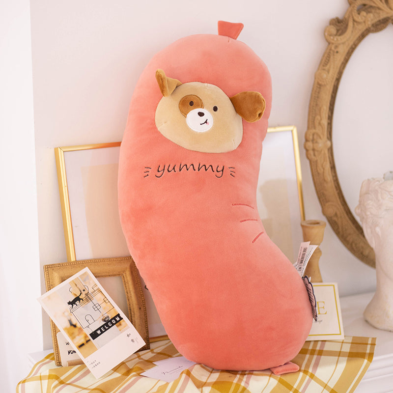One coral-pink bean-shaped plush cushion with beige dog face patch, brown ears and 'yummy' embroidery.
