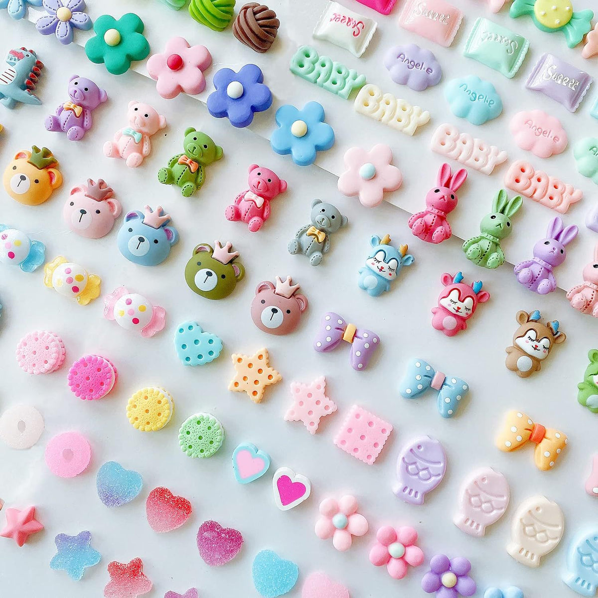 Rows of small pastel resin charms including bears, bunnies, flowers and baby letters on a white surface