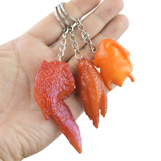 Hand holding three chicken-part keychain charms on silver rings: red wing, orange foot, small orange chicken.