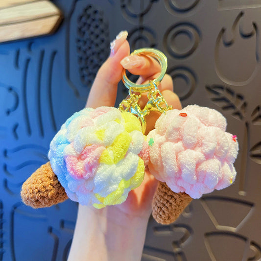 Hand holding two fluffy ice cream cone plush keychains, one rainbow and one pink, with crochet cones