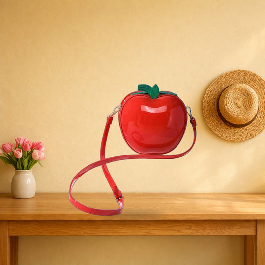 Red apple crossbody bag on an oak hall table, strap draped over the edge