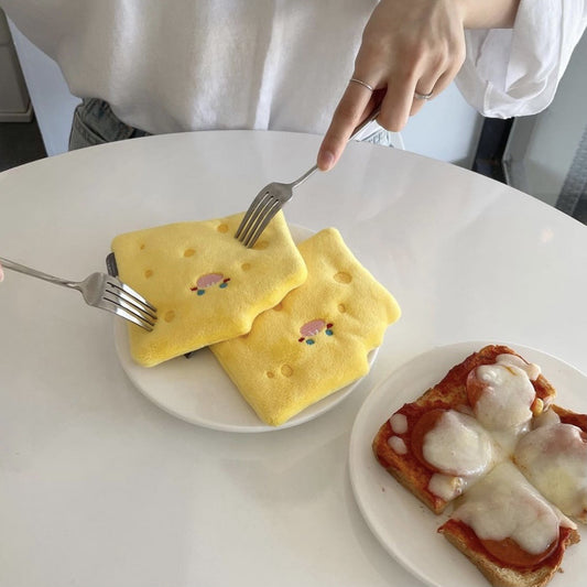 Yellow cheese wedge crinkle dog toy on a white plate, being cut with a fork, next to pizza toast