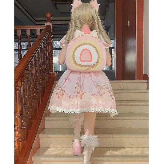 One round pastel-pink backpack with cake-roll swirl and heart center, white bow top, worn by person.