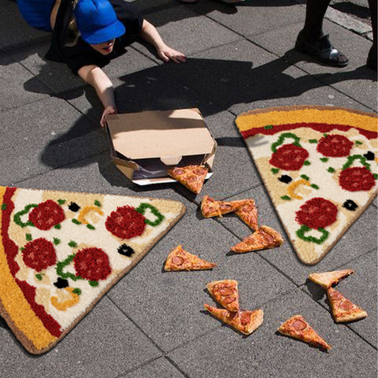 Two large plush pizza slice rugs on pavement beside an open pizza box and real pizza slices