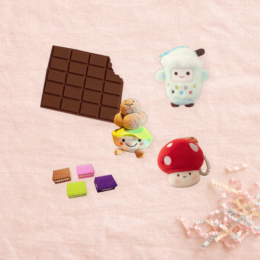 Example lucky bag of five snacks on pink linen: memo pad, bubble tea charm, dim sum charm, biscuit erasers, mushroom charm