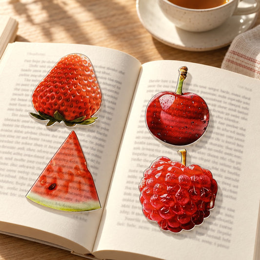 Four fruit bookmarks lying on an open book with the page text showing through the clear acrylic, a cup of tea behind