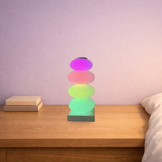 Rainbow candy skewer lamp glowing pink, green and blue on a bedside table