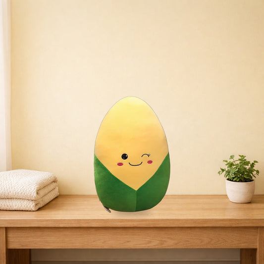 Winking corn plush pillow with green husk sitting on a light oak bench