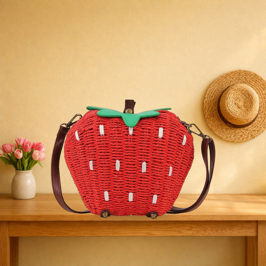 Woven strawberry crossbody bag with its brown strap on an oak hall table