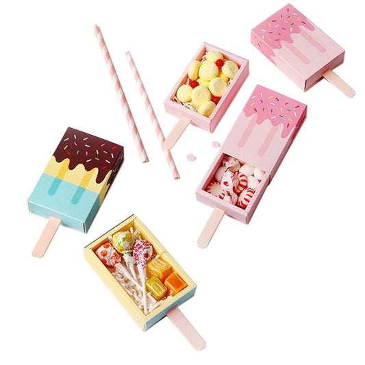 Pink and blue ice lolly party favour boxes, some slid open with sweets inside, beside paper straws