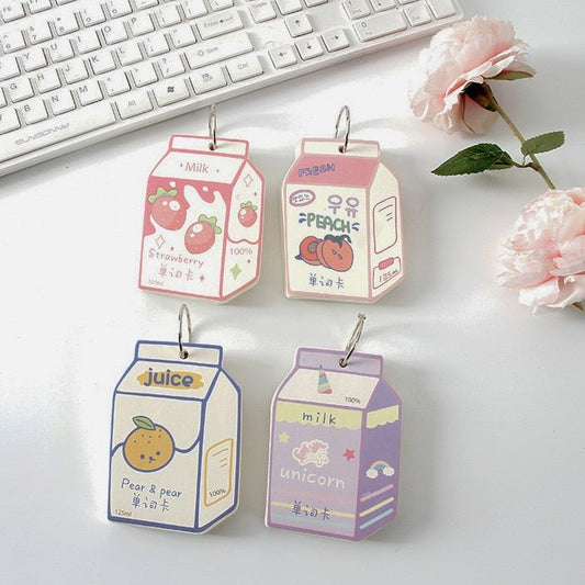Four milk carton mini notebooks in strawberry, peach, juice and milk designs with metal rings on a desk