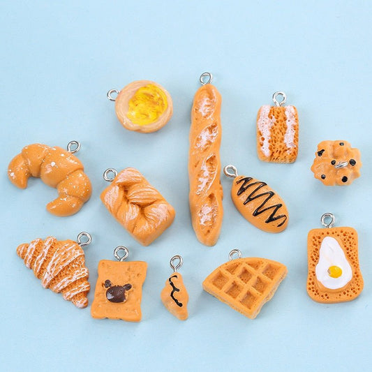 Resin bakery charms laid out on a light blue background, croissant, baguette, egg toast and waffle