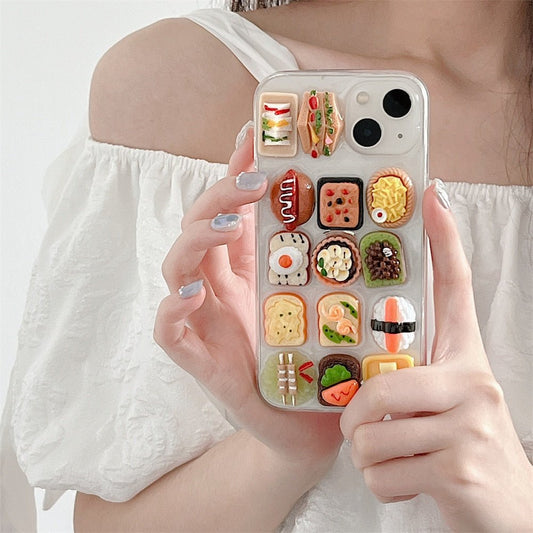 Clear 3D iPhone case with resin sushi, toast and egg food charms held by a person in a white top