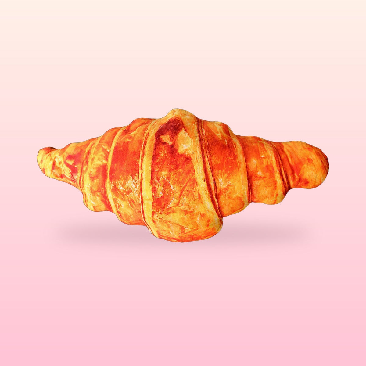 Giant croissant hug pillow with a golden flaky bakery print on a soft pink background