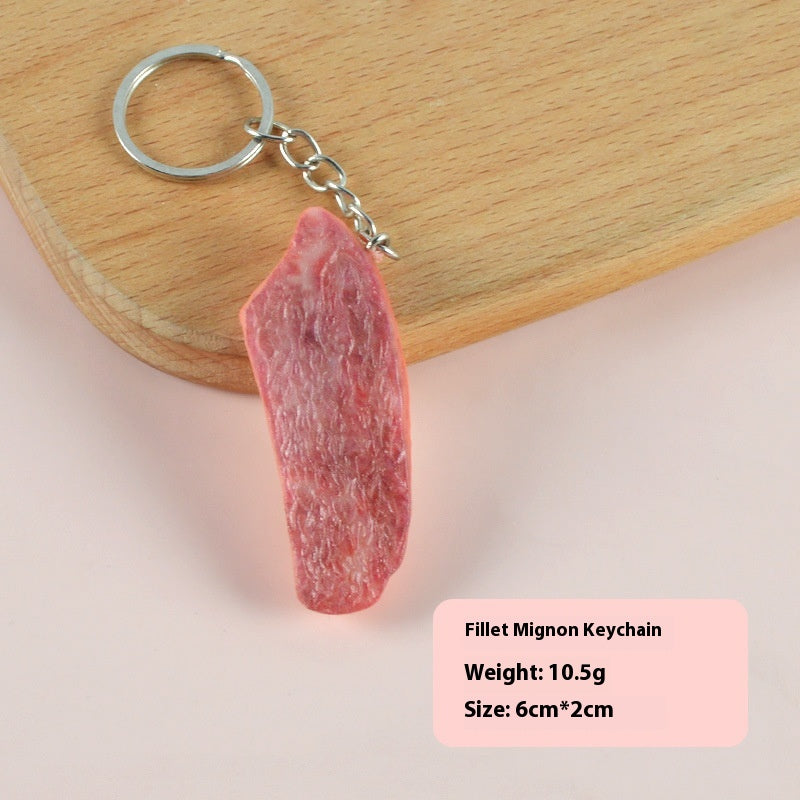 One pink-red fillet-mignon-shaped keychain hanging from a silver split ring and short chain on a wooden board.