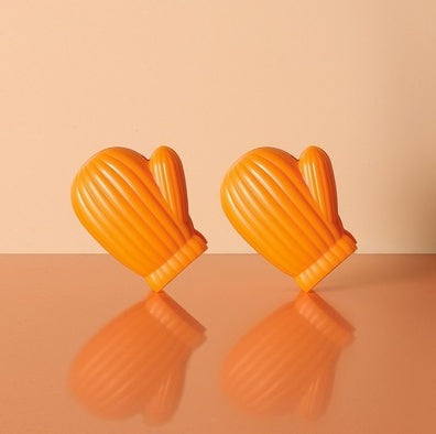 Two orange ribbed mitten-shaped clips standing upright on a glossy peach surface with reflections.