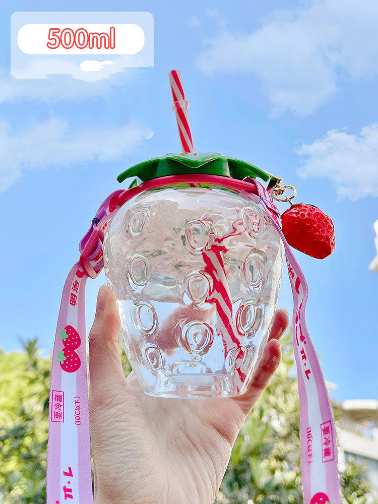 Hand holding 1 clear strawberry-shaped cup with green lid, striped straw, pink lanyard and strawberry charm.