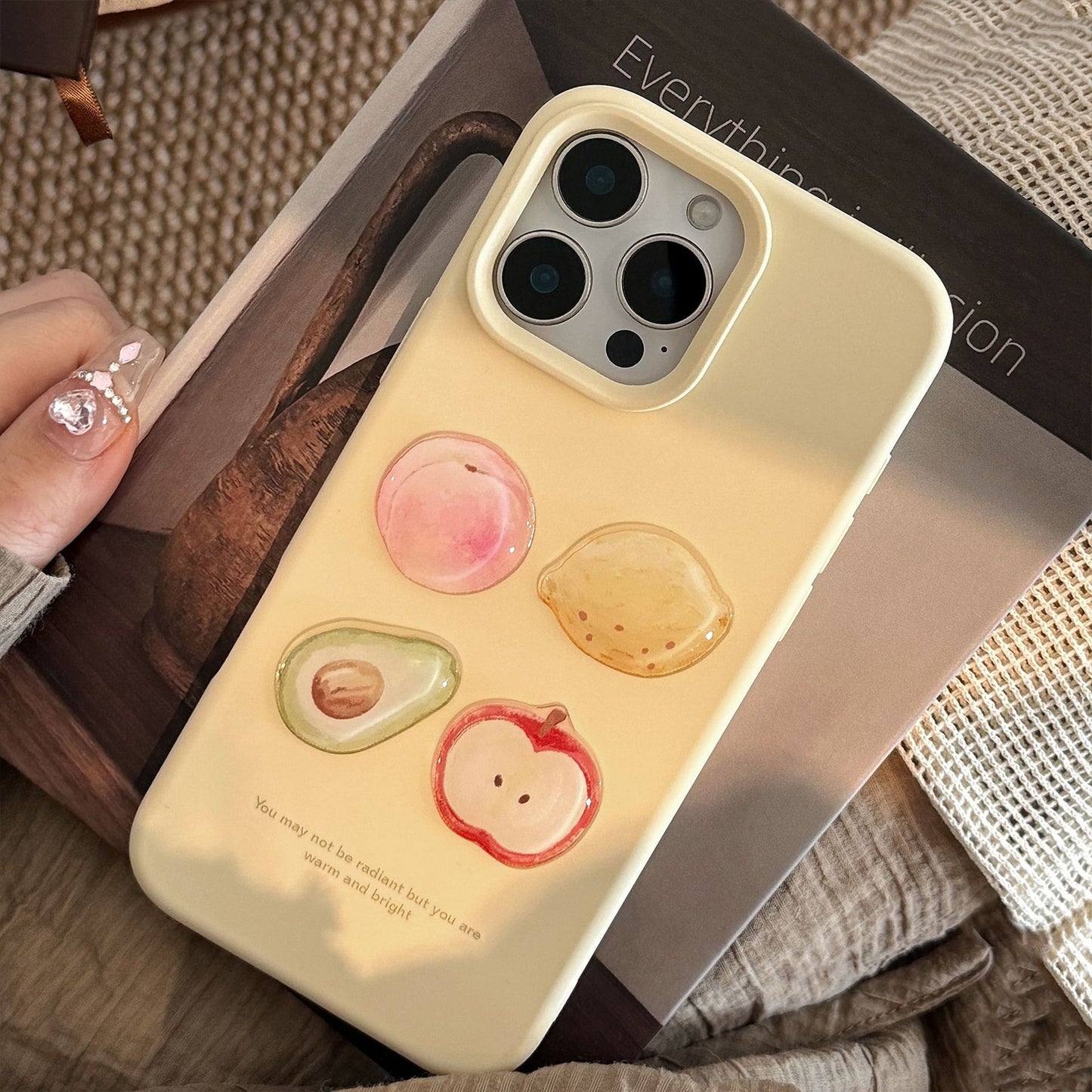 Yellow 3D iPhone case featuring glossy fruit designs: peach, avocado, lemon, and apple, with a motivational quote below.