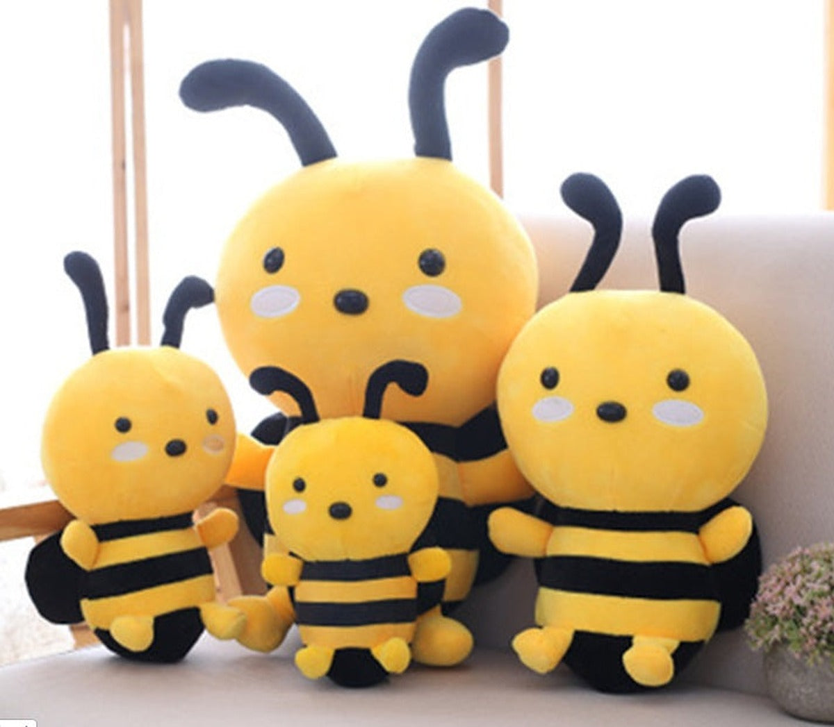 Four yellow and black plush bees in different sizes sitting together on a sofa