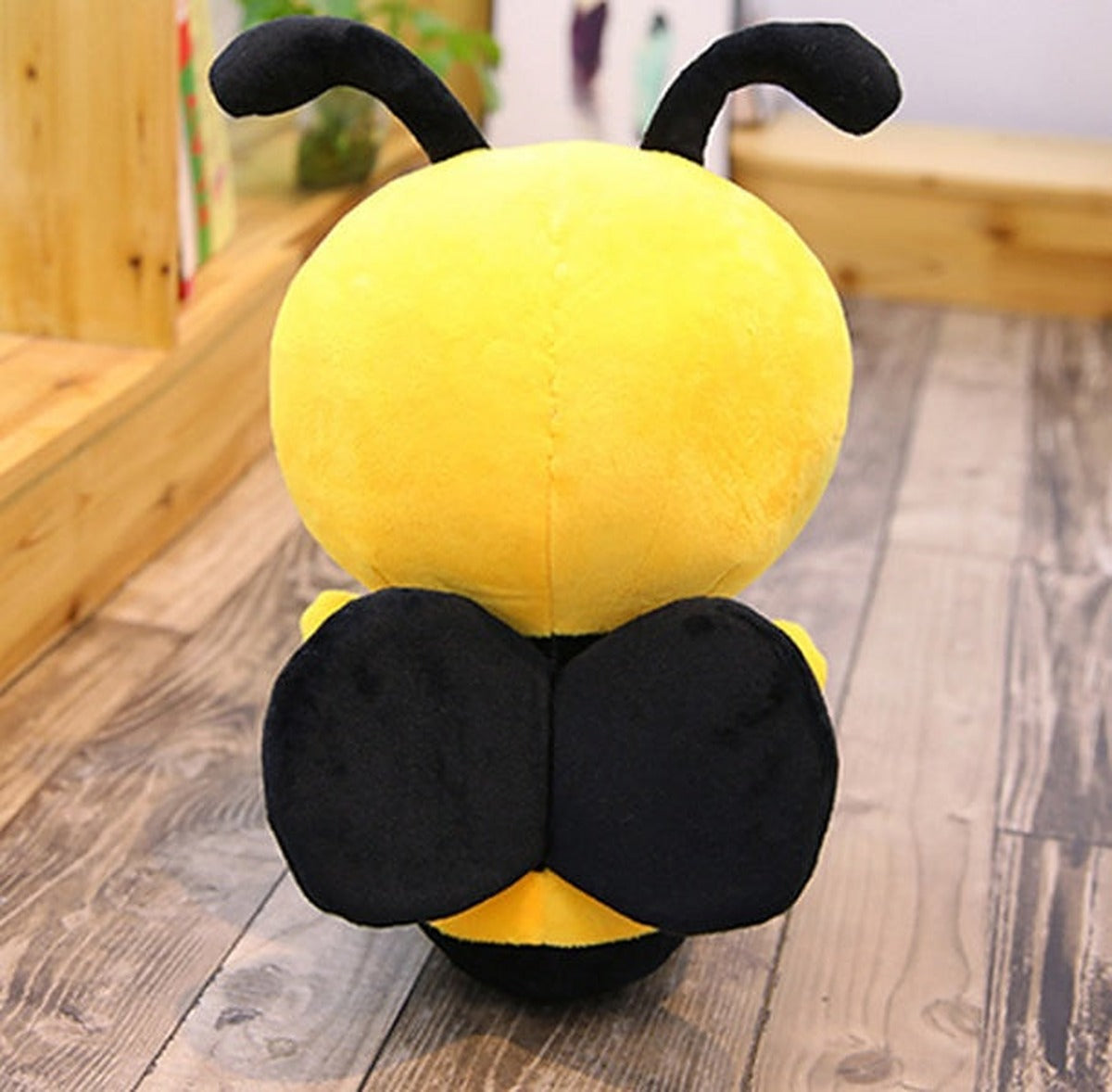 Back view of a yellow and black plush bee with two black wings on a wooden floor