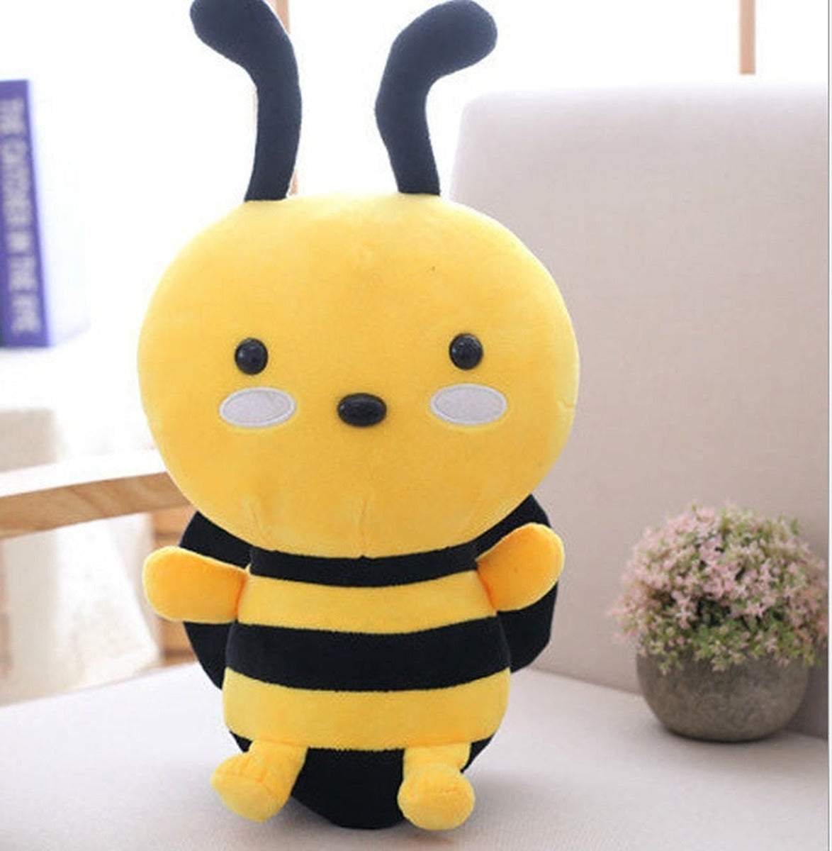Yellow plush bee with black stripes, black antennae and white cheek patches sitting on a sofa