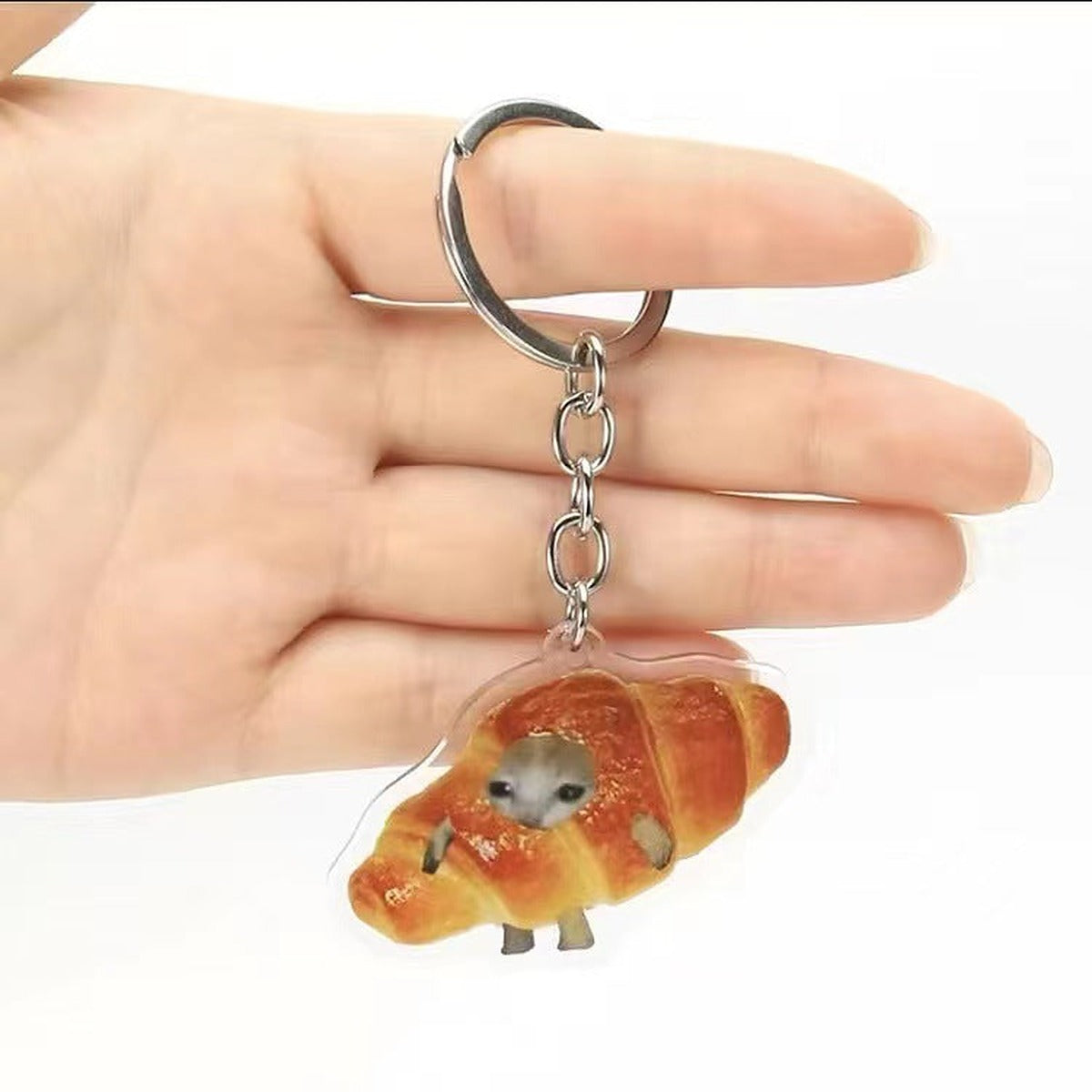 Croissant cat meme acrylic keychain held on a hand