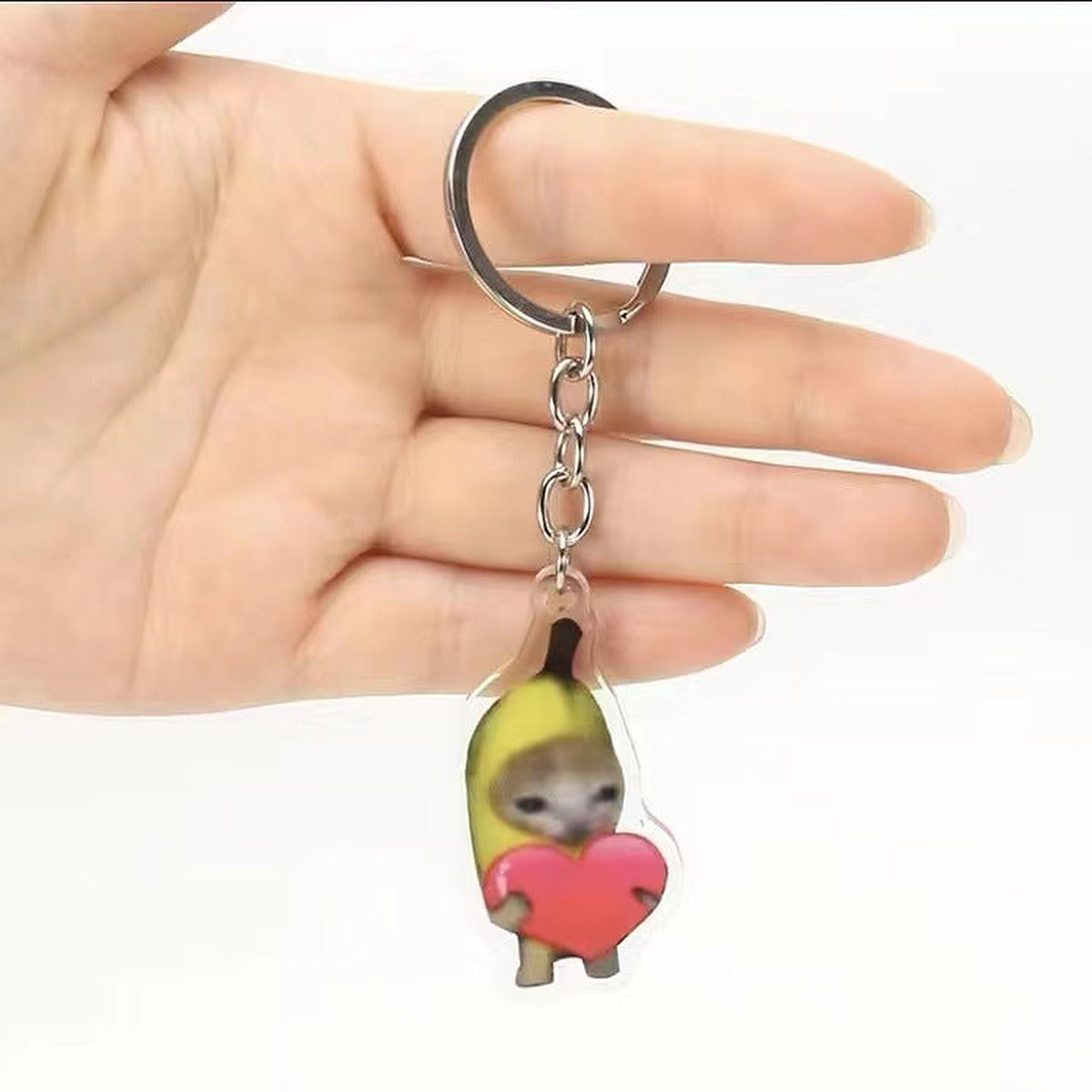 Heart banana cat meme acrylic keychain held on a hand