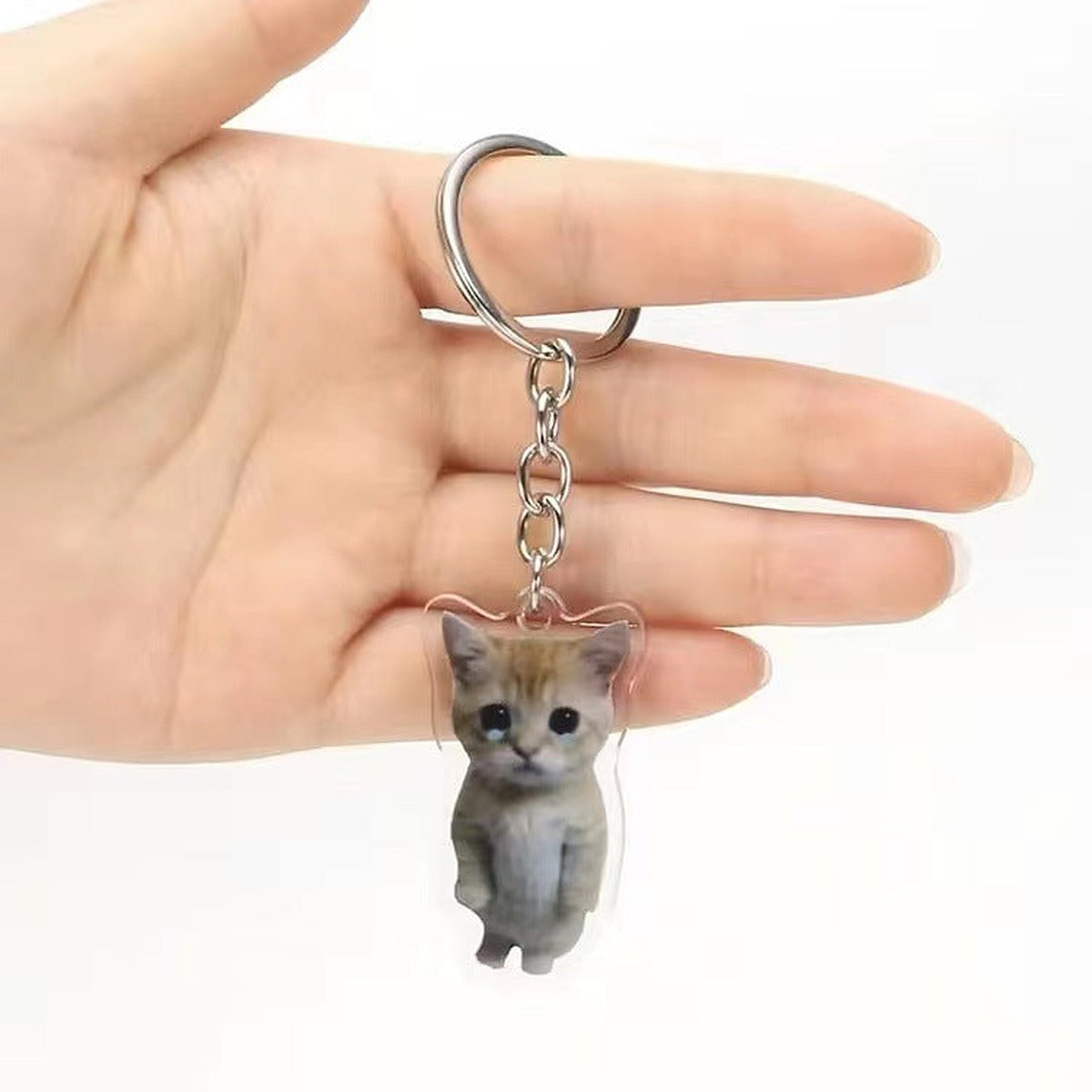 Sad kitten acrylic keychain with a round ring held on a hand