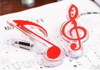 Two clear plastic clips with red musical-note designs (treble clef and eighth note) on sheet music.