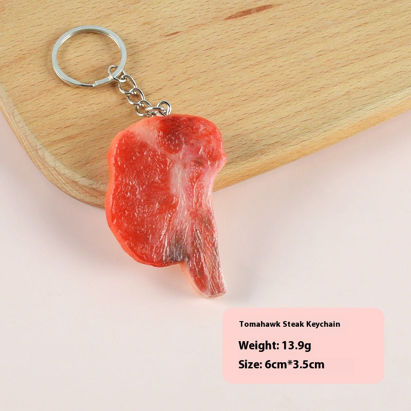 Single red tomahawk steak-shaped keychain with a silver ring and short chain on a wooden cutting board.