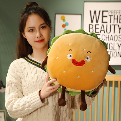 One round hamburger plush cushion with tan bun, sesame seeds, red smile, green lettuce ruffle and brown legs.