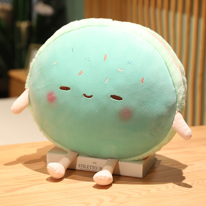 Single round mint-green plush with embroidered sleepy face, sprinkles, pink limbs, sitting on a book.