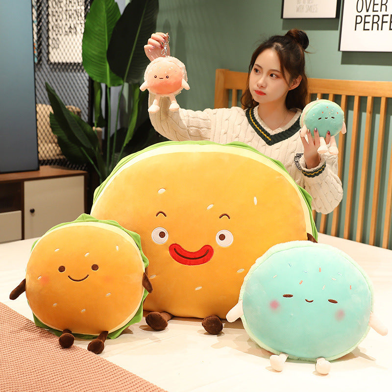 Woman holds two small plush; three larger burger cushions on table: big yellow, orange, mint.