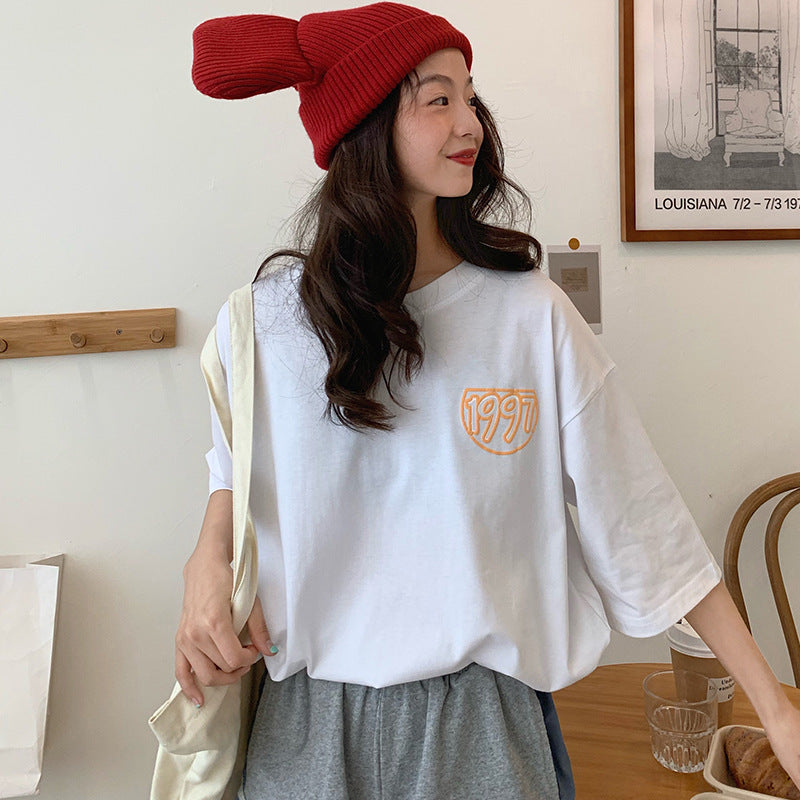 One white oversized T-shirt with orange "1997" chest logo, worn by model with red slouchy beanie.