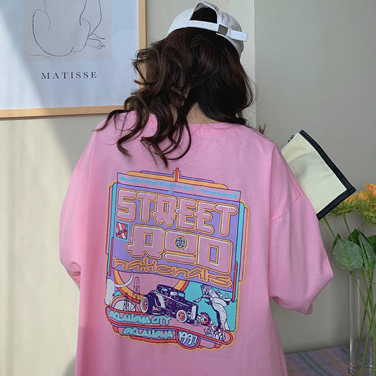 One oversized pink T-shirt shown from back with large multicolored retro car graphic, model wearing white cap.
