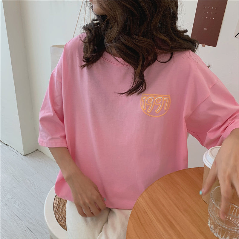 One oversized pink short-sleeve T-shirt on a seated model with yellow "1997" chest logo.