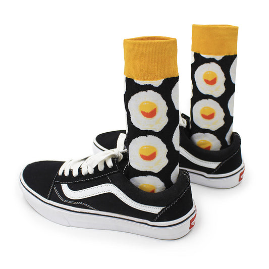 Pair of black crew socks with mustard cuffs and fried-egg pattern inside black-and-white canvas sneakers.