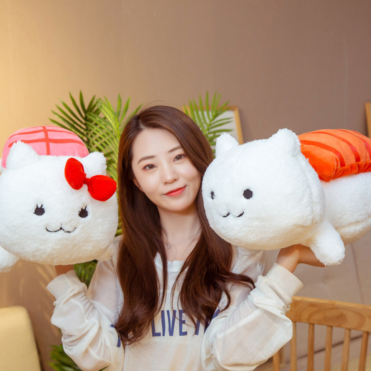 Woman holding two fluffy white cat plushes, one with orange topping and one with pink topping and red bow.