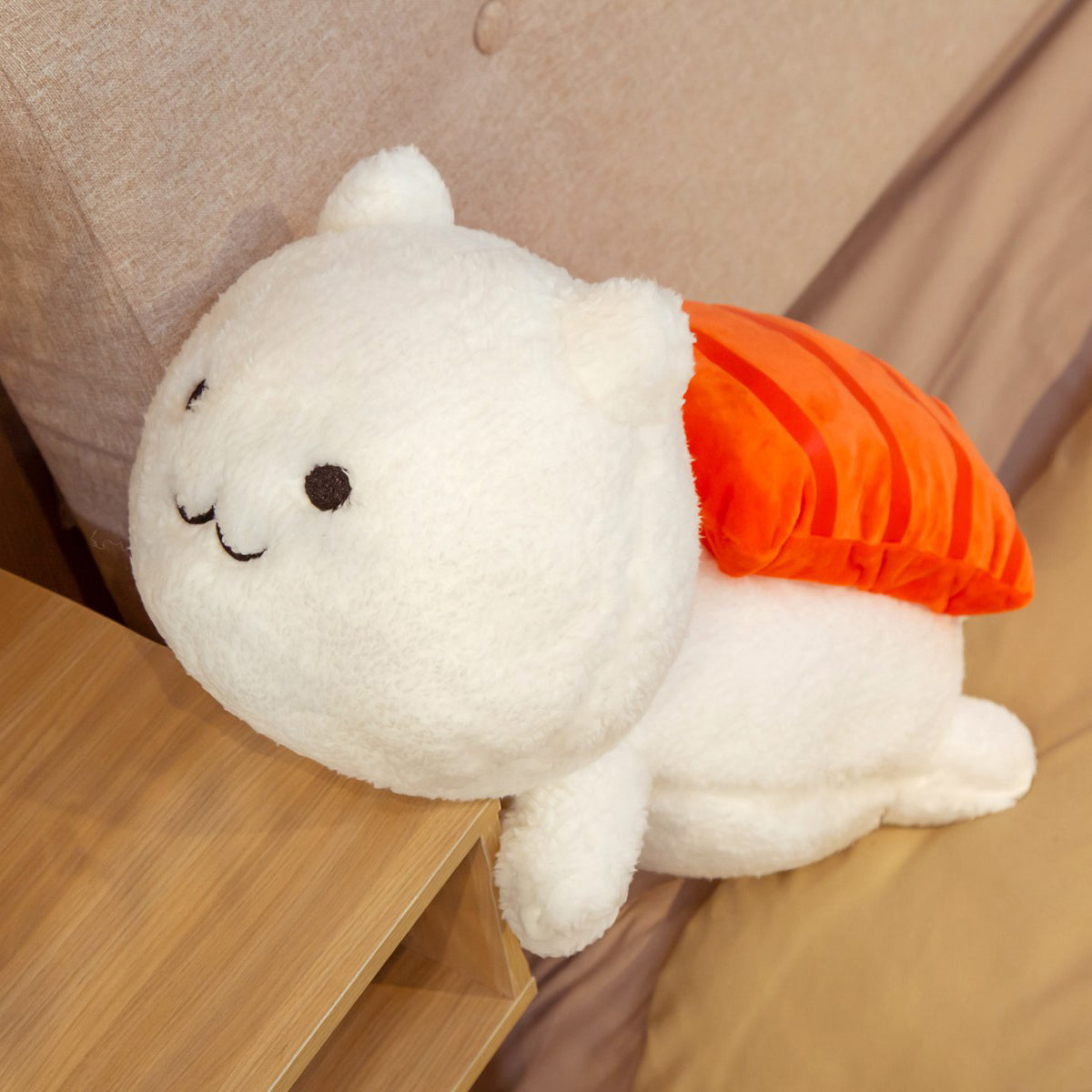 One large white fluffy plush with embroidered face and orange-striped sushi topping, leaning on bedside table.