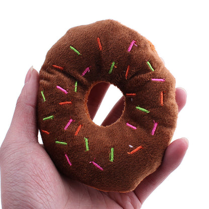 Hand holding one small brown plush donut with pink, green and orange embroidered sprinkles and center hole.
