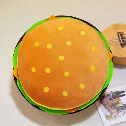 One round hamburger-shaped plush pillow with orange bun and yellow dots, green lettuce, brown patty edges.