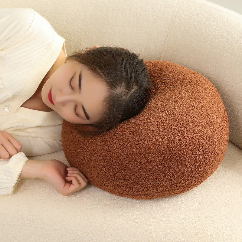 A woman resting her head on one round brown textured cushion on a cream upholstered sofa.