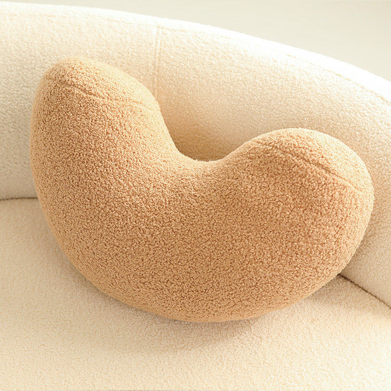 One camel‑tan crescent-shaped cushion with a soft boucle texture resting on a cream upholstered chair.