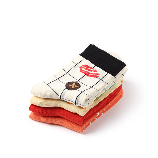 Four folded socks stacked: top cream grid with black cuff and food motifs; below yellow, red and orange.