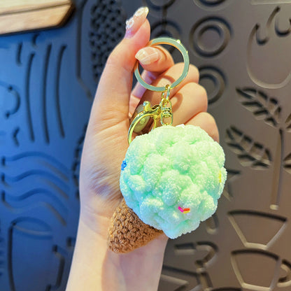 One mint-green fluffy ice cream keychain with brown crocheted cone, tiny sprinkles and gold ring, held in h...