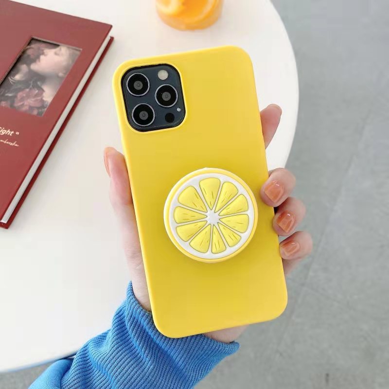 Hand holding one yellow phone case with round lemon-slice grip attached, blue sleeve visible.
