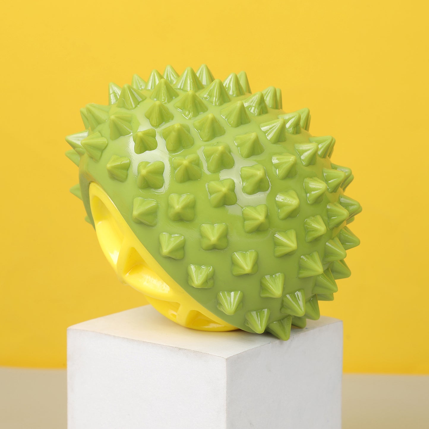 One green glossy spiky rubber chew toy with yellow hollow interior on white block, yellow background.