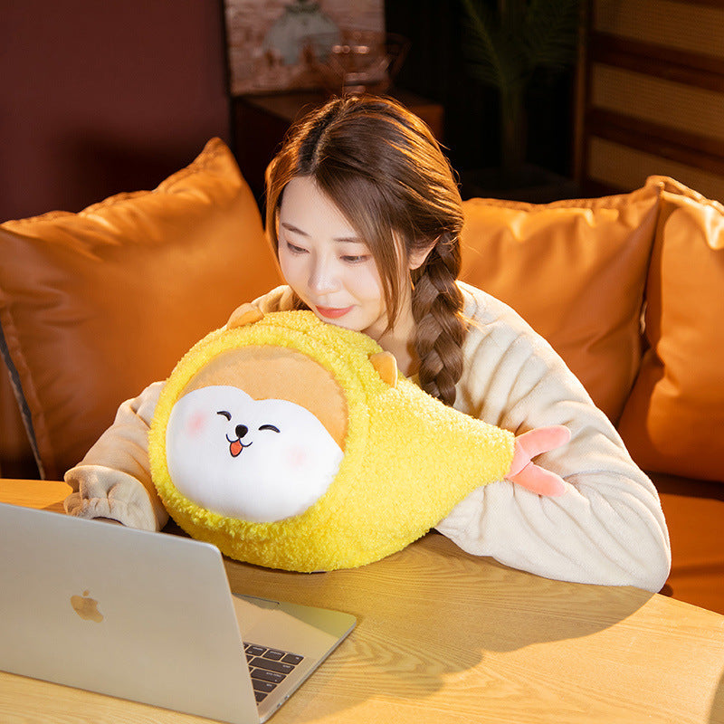 Person hugging one yellow fuzzy plush with a round white smiling face and pink tail at a table with a laptop.