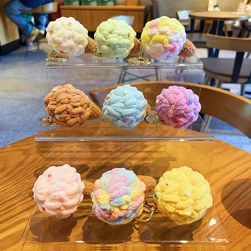 Nine plush ice cream cone keychains with fuzzy pastel scoops, sequin sprinkles and brown cones on clear stand.